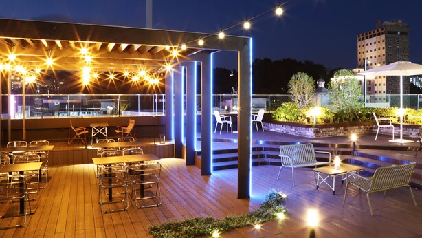 Un área de comedor al aire libre con luces colgantes, mesas y sillas de madera.