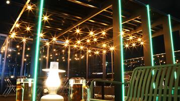 A table with two glasses of beer and a lit lamp, set against a backdrop of a metal structure with star-shaped lights.