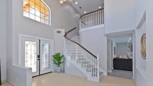 A spacious interior with a polished floor, a staircase with white railings, and a potted plant.