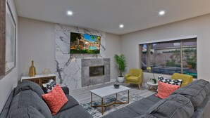 A modern living room with a gray sectional sofa, a white coffee table, a fireplace, and a large window offering a view of the outdoors.