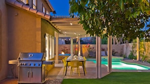 A backyard with a barbecue grill, a dining table with chairs, and a swimming pool.