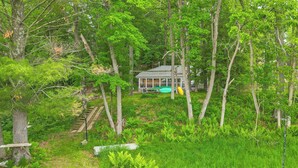 A cabin surrounded by dense forest, with a visible deck and a kayak. - Lakefront Cabin w/ Fire Pit, Dock, & Boat Rental (Augusta)