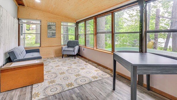 A cozy room with a wooden ceiling, large windows, a gray sofa, a small table, and a patterned rug. - Lakefront Cabin w/ Fire Pit, Dock, & Boat Rental (Augusta)