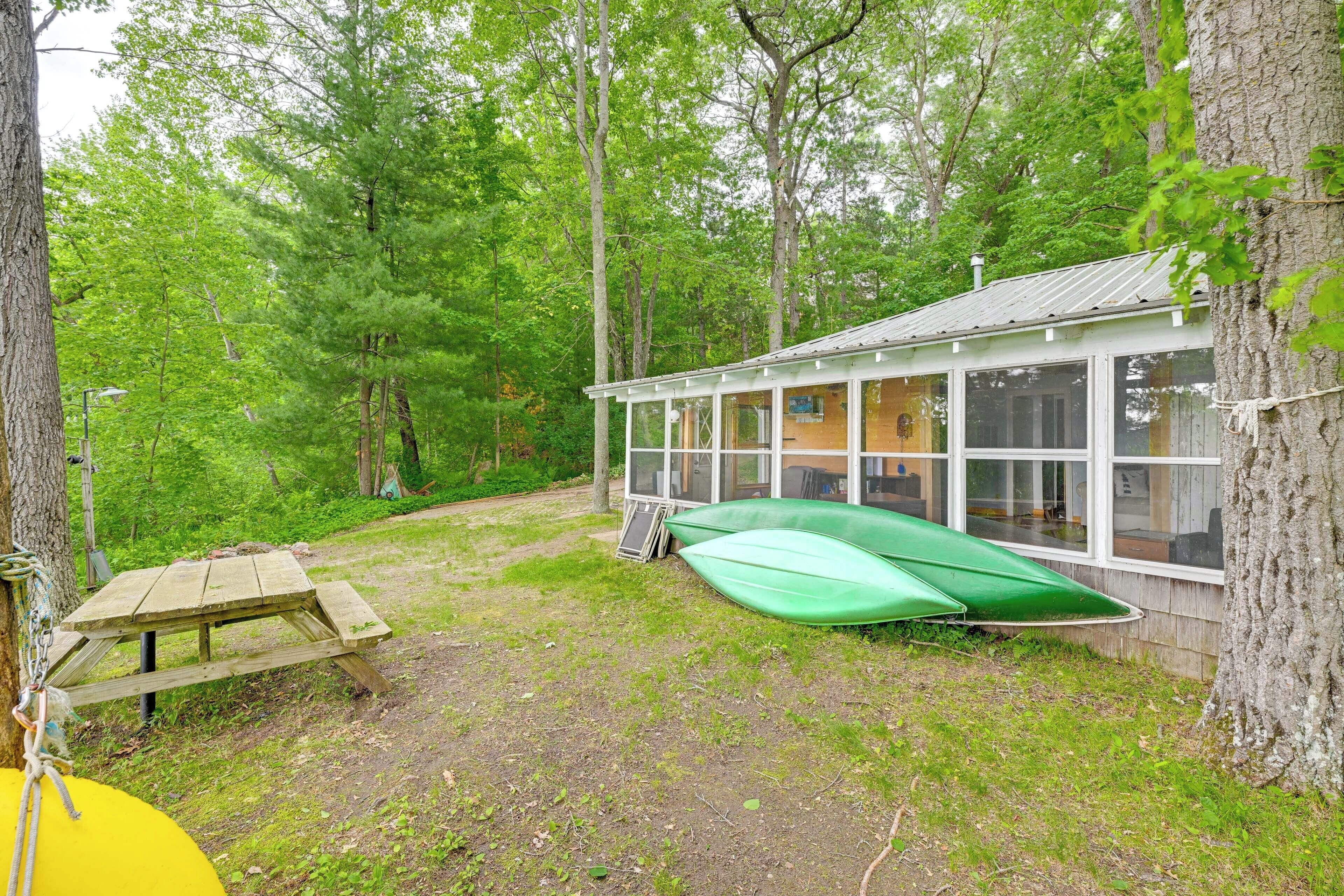 Eine Hütte mit Glasveranda, Picknicktisch und einem grünen Kanu.