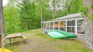Eine Hütte mit Glasveranda, Picknicktisch und einem grünen Kanu.