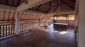 An open-plan interior with high ceilings, wooden beams, and a balcony with a view. - Kemangi Apartments and Yoga Space (Ubud)