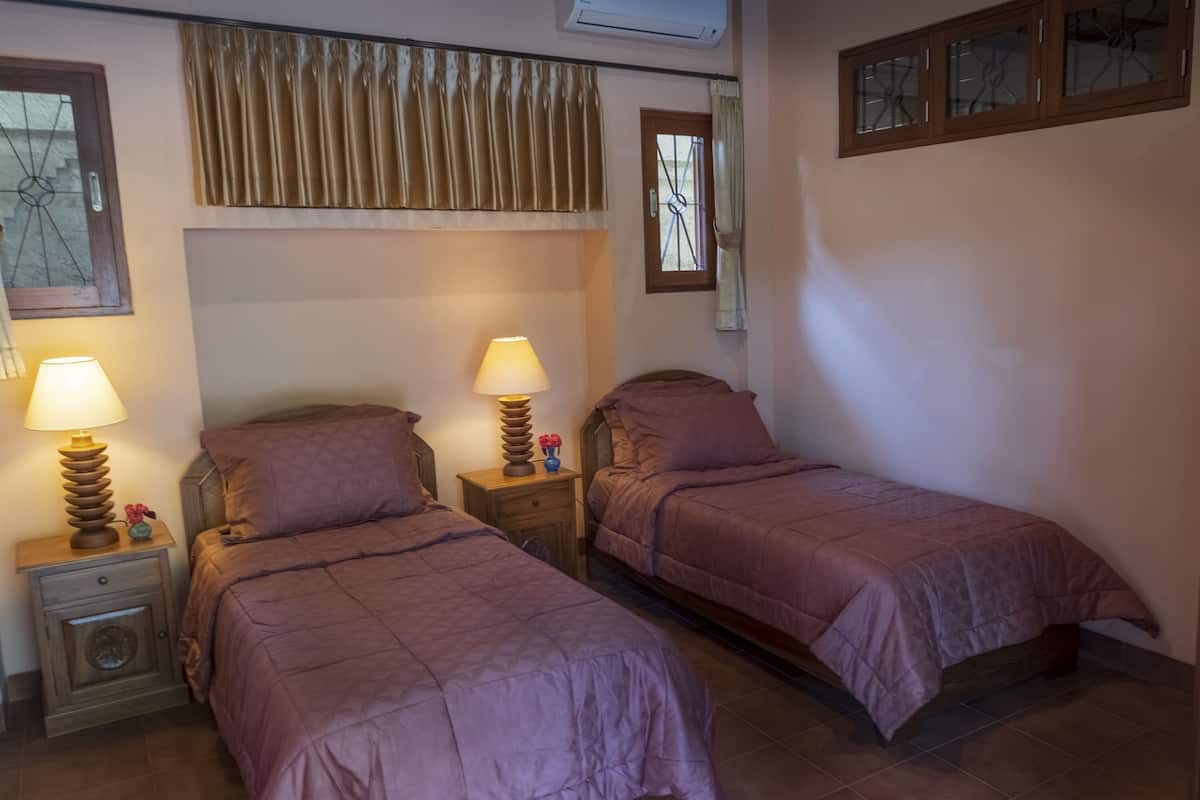 A bedroom with two beds, each with a wooden nightstand and a lamp. There is a window with a curtain and a mirror above the beds.