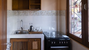 A kitchen with a stove, sink, and wooden cabinets. - Kemangi Apartments and Yoga Space (Ubud)
