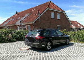 Ein schwarzer Citroën DS parkt vor einem rot Backsteinhaus mit einem geneigten Dach und einer Treppe, die zu einer Tür mit der Aufschrift „Espace“ führt.