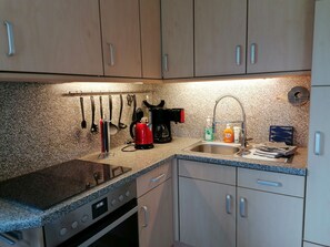 Eine kompakte Küche mit einer Granitarbeitsplatte, einer Edelstahlspüle und einem eingebauten Backofen.