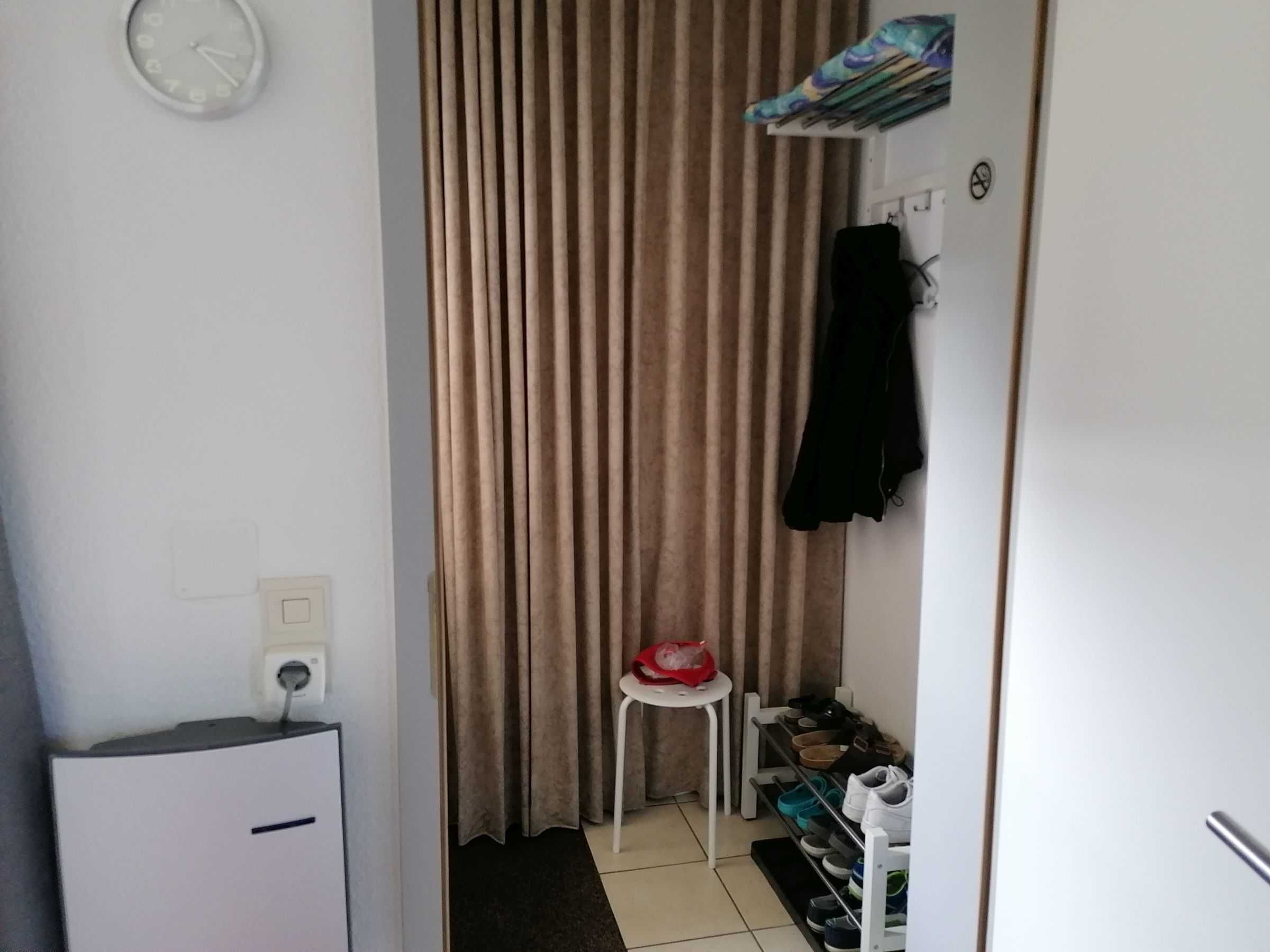 A small, compact room with a white desk, a chair, a coat rack, and a shoe rack.