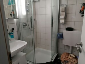 Moderni kylpyhuone, jossa on lasiseinällä varustettu suihku, valkoinen pesuallas ja wc.