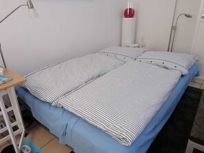 Siististi pedattu sänky, jossa on raidallinen vuodevaatteisto, työpöytä lampun kanssa ja punainen, pallonmuotoinen esine valkoisella jalustalla.