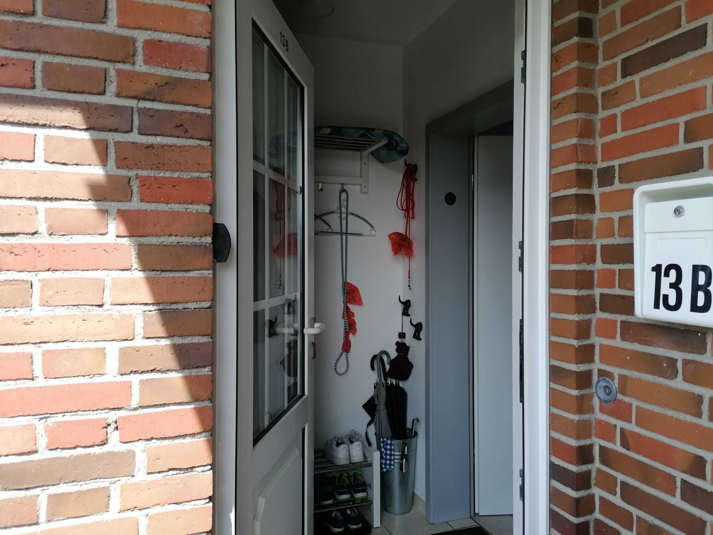 En smal hall med en tegelvägg på ena sidan och en dörr som leder in till ett rum. Ett nummer på väggen, ’13B’, syns tydligt.