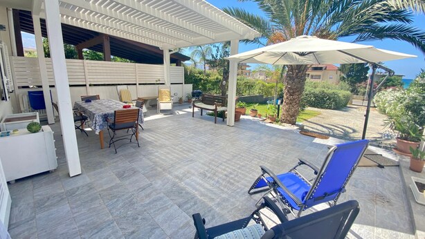 Un patio al aire libre con un área de estar cubierta, una mesa con sillas y plantas en macetas.