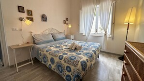 Un dormitorio con cama, mesitas de noche, lámpara y ventana con cortinas.