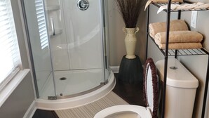 Un baño moderno con ducha de vidrio, inodoro blanco, toallero con toallas y un florero decorativo.