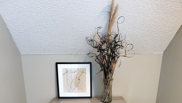 Un rincón con una estantería de madera que contiene toallas dobladas y un florero con plantas secas.