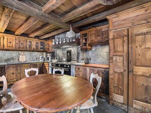 A rustic kitchen with wooden cabinets, a stone wall, and a round wooden table with chairs. - Authentic and spacious chalet with jacuzzi and hammam, near Méribel center (Méribel)