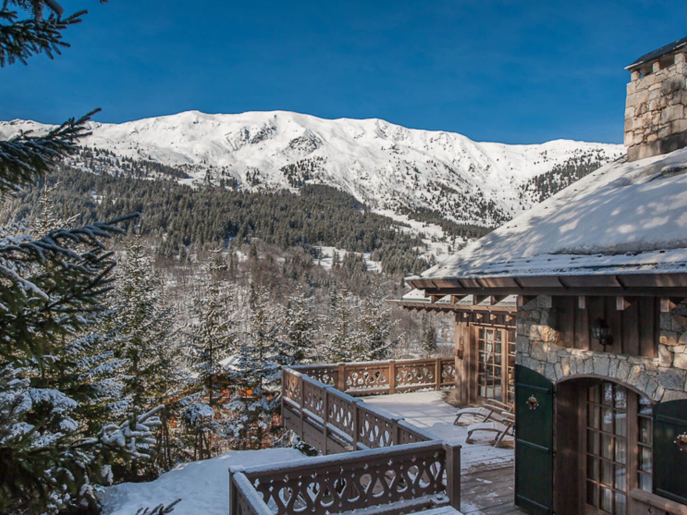 A snow-covered mountain landscape with a wooden building featuring a stone entrance and a balcony overlooking the scenery.