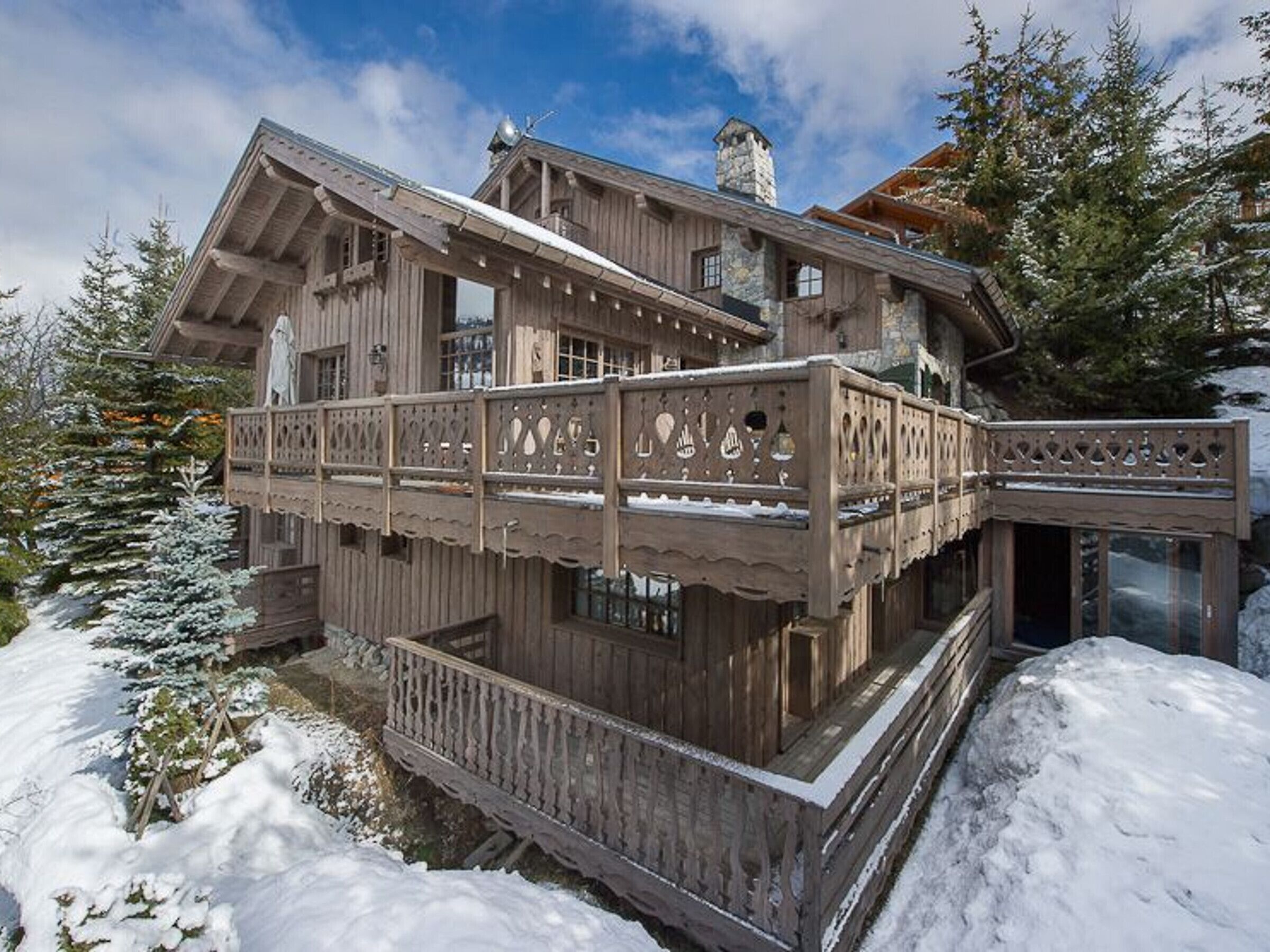 A wooden chalet with a balcony, surrounded by snow-covered trees.
