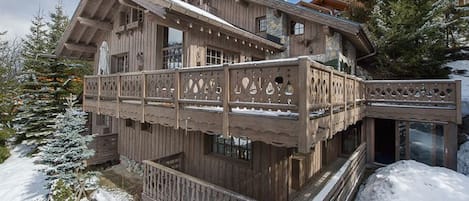 A wooden chalet with a balcony, surrounded by snow-covered trees.