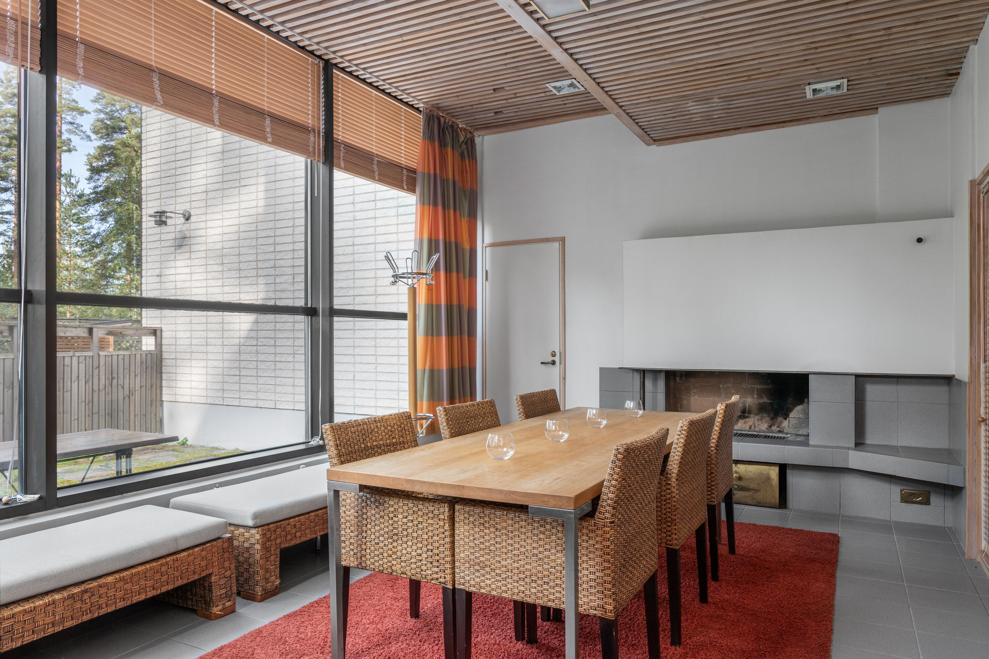 Een moderne eethoek met een houten tafel, rieten stoelen, grote ramen en een open haard.