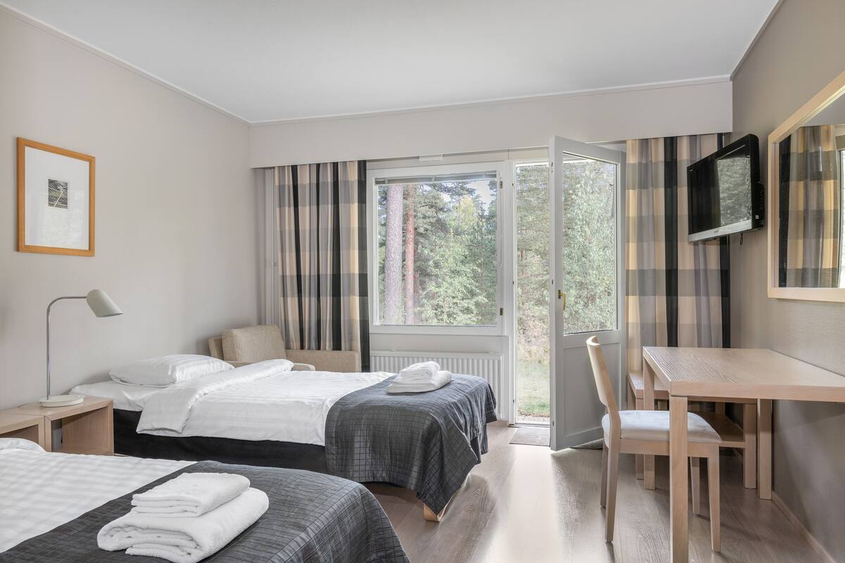 Une chambre d’hôtel avec deux lits, un bureau, une chaise, une télévision et une fenêtre avec des rideaux.