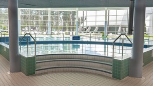 An indoor swimming pool with clear glass walls, large windows, and tiled flooring.