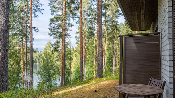 A wooden deck with a table and chair, overlooking a forest and a lake.