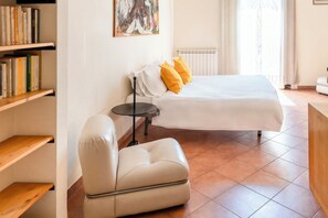 Ein modernes Hotelzimmer mit einem Bett, einem Sessel, einem kleinen Tisch und einem Bücherregal.