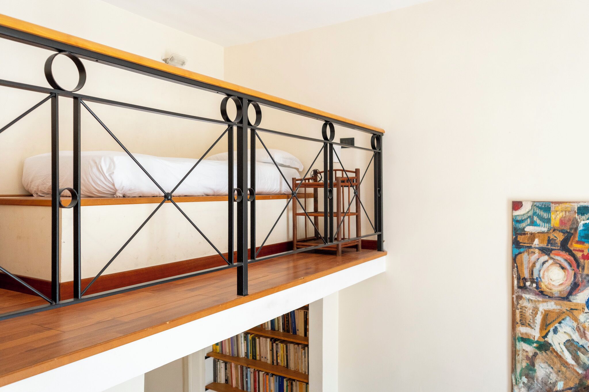 Une chambre aménagée en mezzanine avec un plancher en bois, un lit, une chaise et une bibliothèque.