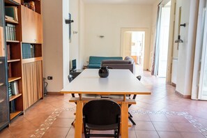 Ein Zimmer mit einem großen Holztisch, einem schwarzen Stuhl, einem türkisgrünen Sofa und einer Bücherwand voller Bücher.
