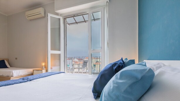 A hotel room with a bed, a bedside table with a lamp, and a balcony with a view of buildings. - Apartment with a View in the Lingotto Area by Wonderful Italy (Turin)