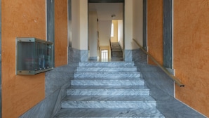 A marble staircase leading to a landing with a glass elevator on the left. - Apartment with a View in the Lingotto Area by Wonderful Italy (Turin)