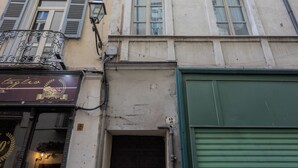 Fachada de edificio con letrero de tienda, una puerta con persiana verde y una ventana con contraventanas.