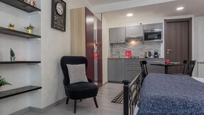 Una habitación de hotel moderna con cama, una silla, una mesita, una zona de cocina y un reloj en la pared.