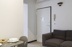 Ein Zimmer mit Esstisch für zwei Personen, einer Couch, einer Tür mit aufgehängtem Handtuch und einem an der Wand befestigten Telefon.