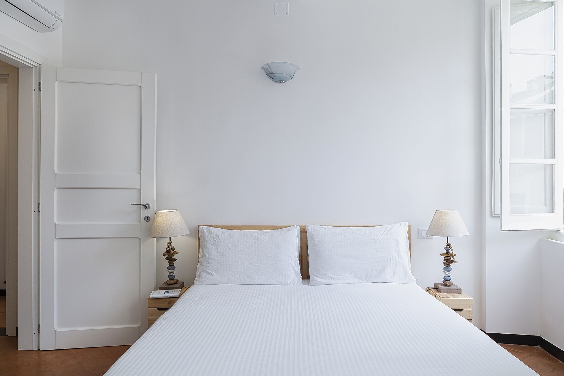 Ein Schlafzimmer mit einem Bett, zwei Nachttischen, einer Wandlampe, einer Tür und einem Fenster.