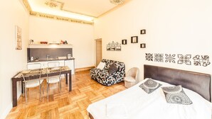 Una habitación de hotel moderna con piso de madera, una cama con almohadas estampadas, un escritorio con sillas, un sofá y decoración de pared.