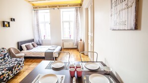 Una habitación bien iluminada con una cama, una mesa de comedor preparada para cuatro personas y una zona de estar acogedora con un sofá estampado.