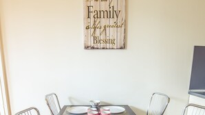Mesa de comedor lista con platos, cubiertos y tazas rosas, rodeada de sillas metálicas.
