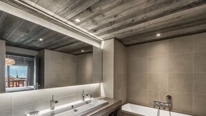Et moderne badeværelse med træloft, stort spejl, to håndvaske og et badekar.