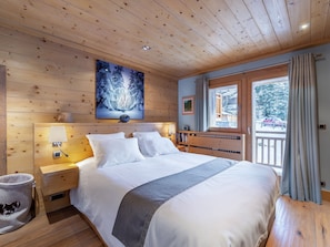 Quarto de cabana de madeira com uma cama grande, uma mesa de cabeceira, uma luminária, um quadro emoldurado e uma janela com cortinas.