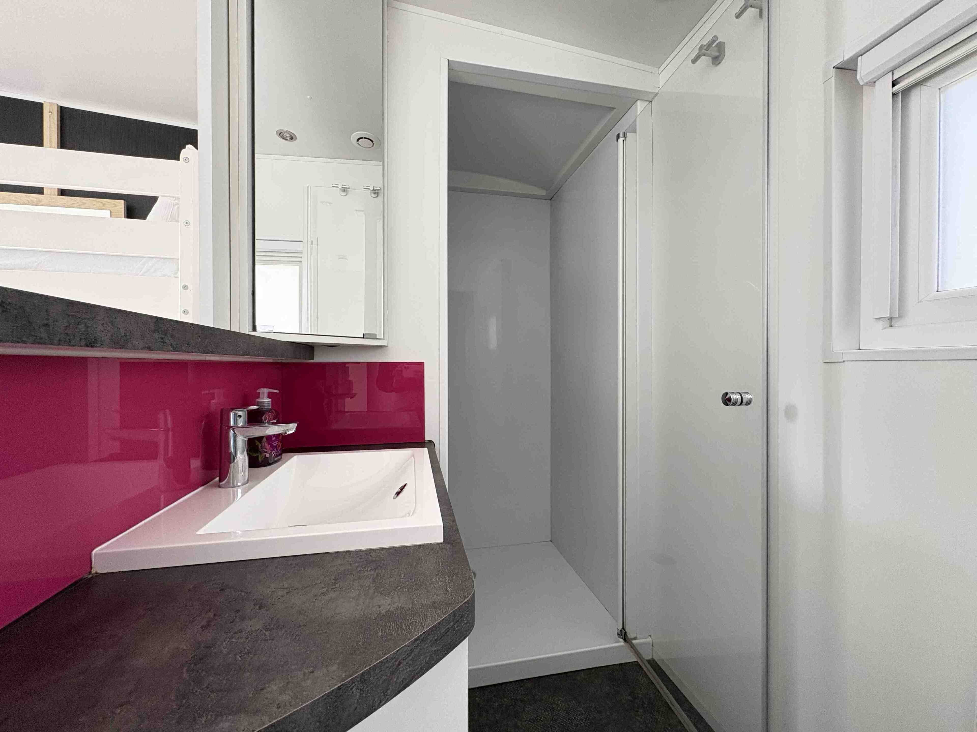 A modern bathroom with a white sink, a pink countertop, and a glass shower enclosure.