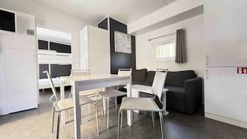 Una habitación compacta y moderna con kitchenette, zona de comedor con mesa y sillas, sofá y ventana pequeña.