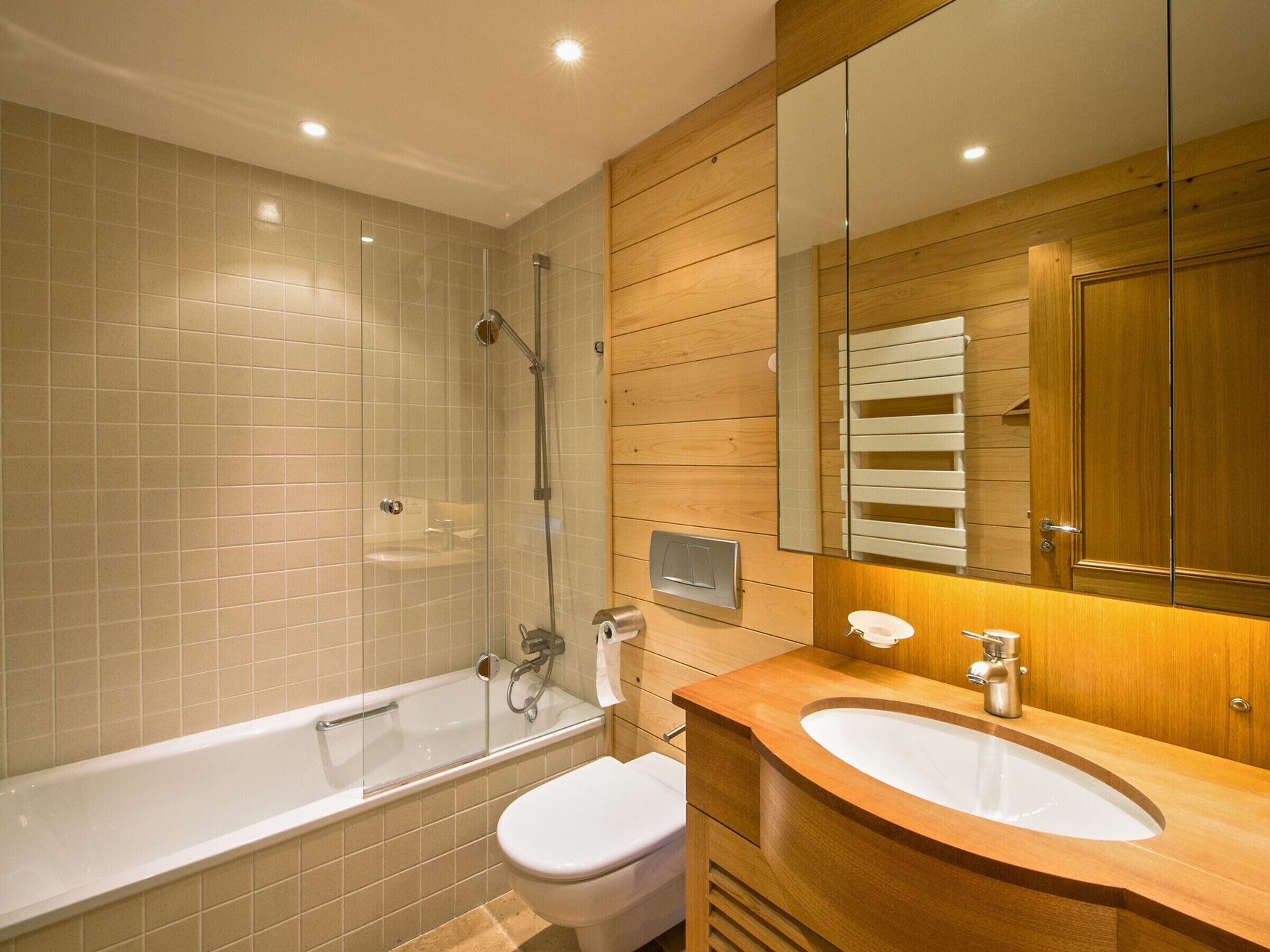 A modern bathroom with a glass-enclosed shower, a white toilet, and a wooden vanity with a sink.
