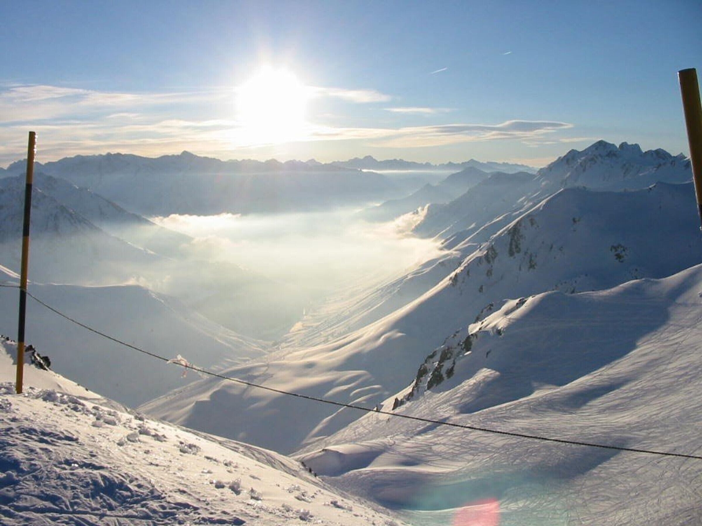 A snow-covered mountain landscape with a clear sky and a sun shining.