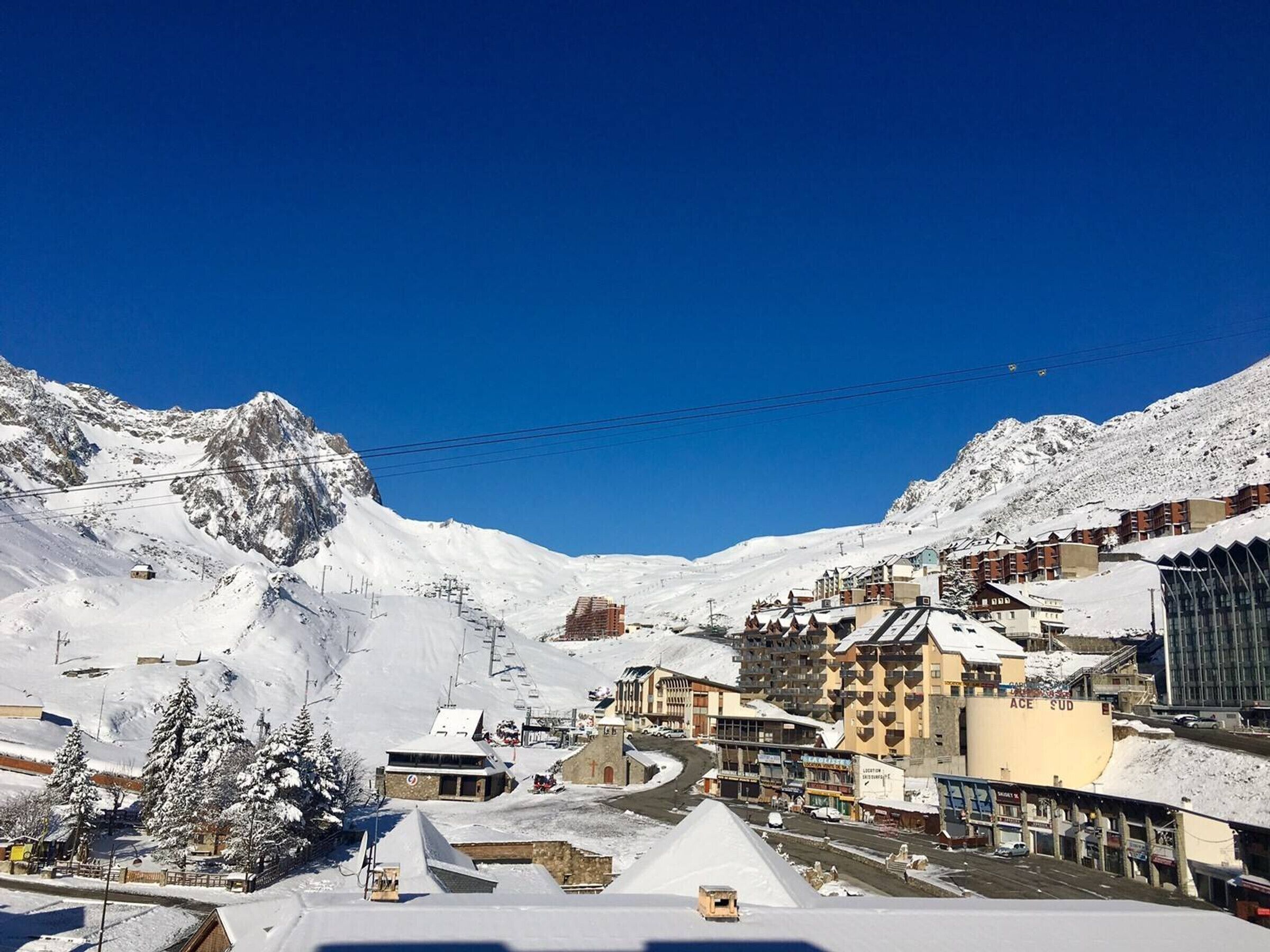Un pueblo cubierto de nieve en la montaña con un telesilla, edificios con balcones y una iglesia.