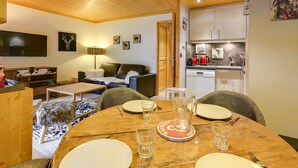 Ett mysigt vardagsrum med ett träpanelat tak, en tv, en soffa och ett matbord för två personer.